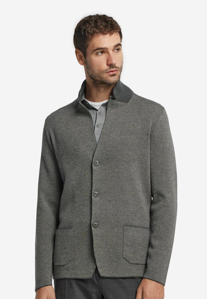 Grå stickad cardigan med en strukturerad yta, fyra knappar, två framfickor och en kontrasterande krage. Avslappnad, modern design.