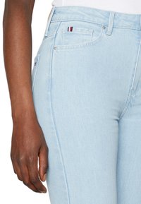 Vaaleansiniset farkut, joissa on korkeavyötärö, etutaskut ja pieni punavalkosinisin raidoin koristeltu merkki takataskun lähellä.