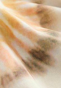 Bomullstextil med ett tie-dye mönster i nyanser av orange, kräm och brunt, som visar en mjuk, texturerad yta med subtil färgblandning.