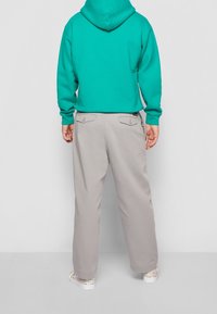 Tyrkysová mikina s kapucí a stahovací šňůrkou, spárovaná se světle šedými kalhotami s širokými nohavicemi a vzorovanými teniskami, které mají detaily na zadní kapse.