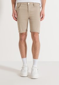 Beige denim shorts met een slim fit, omslagen aan de zomen, voorzakken en ritsluiting. Draag met witte sneakers en enkelsokken.