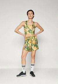 Conjunto deportivo que incluye un top corto y pantalones cortos, ambos con un vibrante patrón floral amarillo. Incluye zapatillas deportivas negras y calcetines.