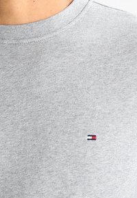 Sudadera de algodón gris con cuello redondo y un pequeño logo bordado en rojo, blanco y azul en la parte izquierda del pecho.