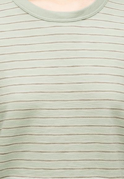 Ανοιχτό πράσινο μπλουζάκι με στρογγυλή λαιμόκοψη και λεπτές οριζόντιες καφέ ρίγες, απεικονιζόμενο από το πάνω μέρος του στήθους έως την περιοχή του λαιμού.