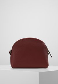 Rote Leder-Zipper-Tasche mit runder Form, strukturiertem Oberflächenfinish und einem kleinen Reißverschlussanhänger. Kompaktes Design, geeignet für verschiedene Aufbewahrungsbedürfnisse.
