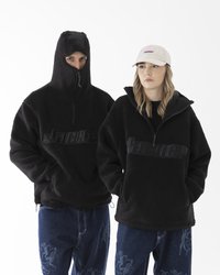 Pullover in pile nero con colletto alto, dotato di chiusura a zip e scritta del marchio in rilievo. Indossato con jeans blu con motivi sottili.