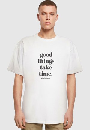 White cotton t-shirt featuring a large black text print that reads "good things take time." with a hashtag below. Loose fit design.