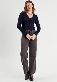 Cárdigan de manga larga azul marino con escote en V, cierre de botones y textura de canalé; combinado con jeans gris de cintura alta y botas negras hasta el tobillo.