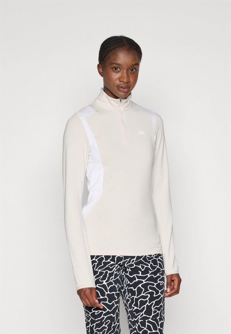 Licht beige sporttop met hoge kraag en halve rits, met witte zijpanelen. Gecombineerd met zwart-wit gestreepte legging.