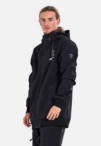 Black zip-up hoodie made of soft fabric. Features a hood, logo prints, and ribbed cuffs. Design is relaxed fit with side pockets.