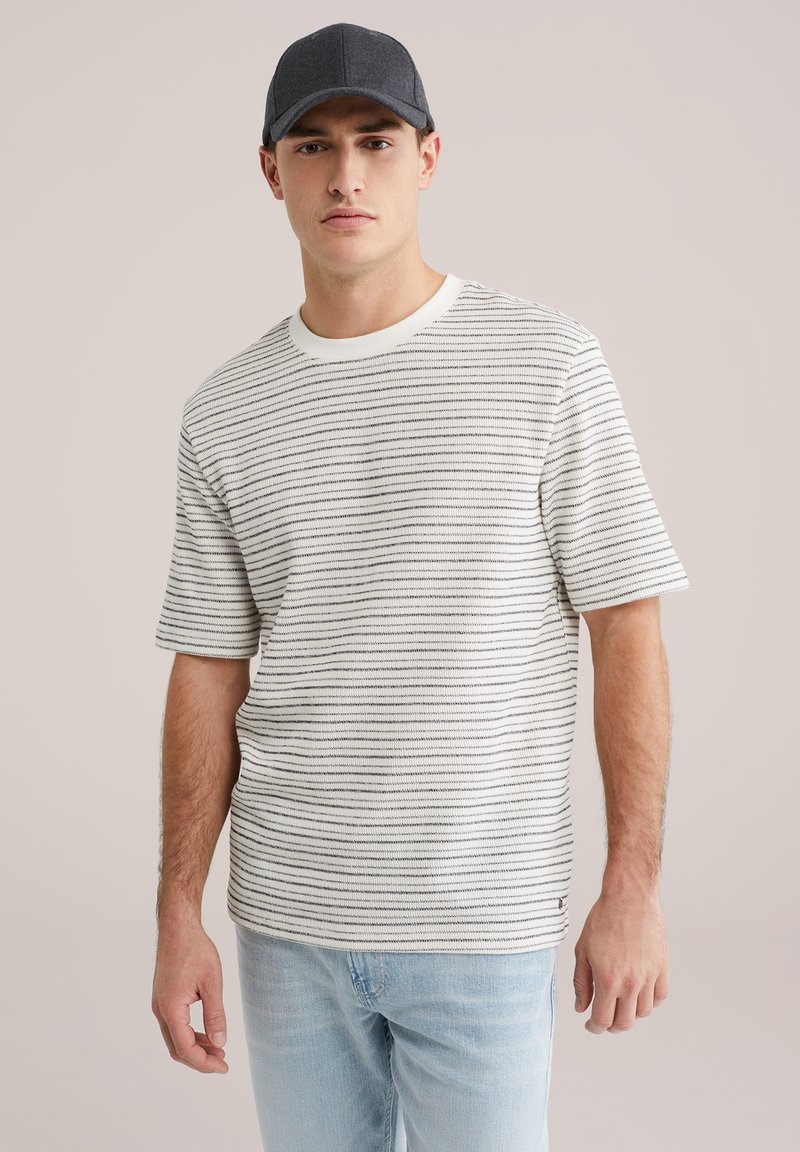 Lühikeste varrukatega valge triibuline T-särk mustade horisontaalsete triipudega, soonikkoes ümarsärg, lõdvestunud istuvus, kombineeritud hele siniste teksadega.