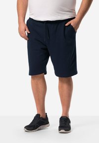 Pantaloni sportivi blu navy in tessuto leggero, con vita elastica e cordino, tasche laterali e una vestibilità ampia. Indossati con scarpe da ginnastica nere.