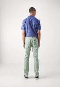 Camisa de manga corta azul combinada con pantalones verde claro, con un ajuste relajado y detalles de bolsillo visibles. El conjunto incluye calzado negro y verde.