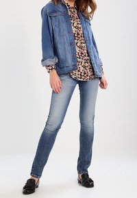 Jeansjacka i ljusblått med två bröstfickor, blommig blus med små rosa och gula blommor, slim-fit blå jeans och svarta loafers.