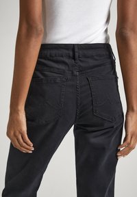 Pantalones de mezclilla negra con cintura alta, que cuentan con dos bolsillos traseros y detalles de costura visibles. La tela tiene una textura suave.