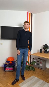 Marineblauer Reißverschluss-Polo-Pullover kombiniert mit hellblauen Jeans und dunkelbraunen Schuhen. Modernes Wohnzimmer mit bunten Wandakzenten und Dekorationsartikeln.