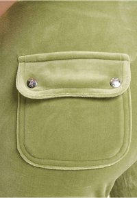 Fleecowa tkanina w oliwkowym kolorze z kieszonką na klapie z detalami w srebrnym kolorze oraz miękką, teksturowaną powierzchnią.