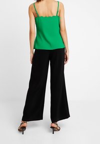 Top senza maniche verde con orlo a scollop, con spalline sottili, abbinato a pantaloni neri larghi e sciolti. Sandali neri con tacco completano l'outfit.