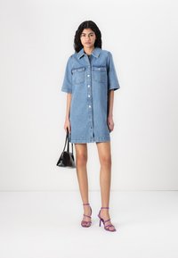 Τζιν φόρεμα σε ανοιχτό μπλε χρώμα με κλείσιμο με κουμπιά, κοντά μανίκια και δύο θήκες στο στήθος. Συνδυασμένο με μοβ σανδάλια με λουριά και μαύρη τσάντα.