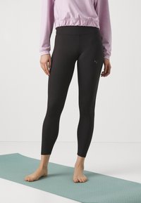 Mustad kõrge vöökoha ja elastse kangaga mustad legginsid. Sile tekstuur, külgõmblused ja diskreetne logo vasakul reiel.