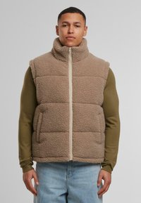 Beige színű fleece mellény magas gallérral, elülső cipzárral és két oldalsó zsebbel. Puha, texturált felületével és téglalap alakú steppelt mintázatával készült.