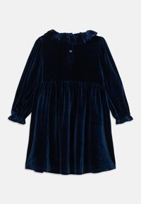 Granatowa welurowa sukienka z długim rękawem, z falbaniastym kołnierzem i mankietami, zapinana na guziki na plecach przy dekolcie.