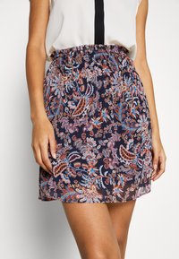 Blommönstrad kjol med elastisk midjeband, med en marinblå bakgrund och flerfärgad paisleymönster. Lätt, genomskinligt tyg.