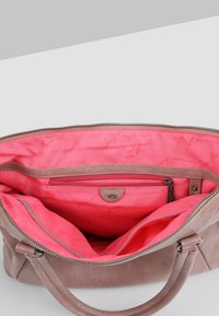 Jasnobrązowa skórzana torebka o gładkiej teksturze. Wnętrze wyściełane żywym różowym materiałem, z kieszenią na zamek i wieloma przegródkami.