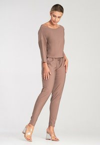Brown, long-sleeve top with a round neck paired with matching tapered pants. Material appears soft and smooth. Clear heeled sandals complete the outfit.
