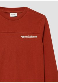 Rdzawy longsleeve z prążkowanym kołnierzem, z małym białym napisem "SPĘDZANIE DNIA W NATURZE" oraz metką marki s.Oliver w kołnierzu.