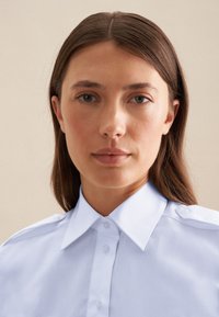 Lichtblauwe geknoopte blouse met knoopsluitingen, gladde textuur en schouderaccenten. De stof lijkt van katoen of een katoenmix te zijn, en heeft een aansluitende pasvorm.