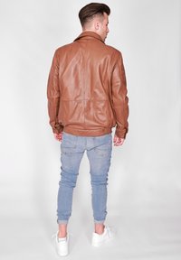 Brun läderjacka med en slät textur, med krage och ribbade muddar, bärs över ljusblå åtsittande jeans och vita sneakers.