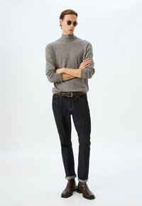 Grå polotröja, mörkblå jeans, vikta ärmslut, brun bälte, bruna ankelstövlar och runda gröna solglasögon. Enkelt, modernt design.