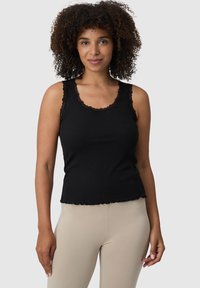 Czarny top na ramiączkach z koronkowym wykończeniem, prążkowaną teksturą i falbaniastym dołem. W połączeniu z beżowymi legginsami. Neutralne tło.