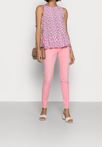 Top peplum senza maniche con un motivo geometrico rosa, abbinato a jeans skinny rosa chiaro e sandali beige con tacco a sorpresa, insieme a una borsa piccola.
