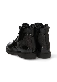 Botines de charol negro con un panel de tela negra texturizada en el lateral, puntera redonda y suela de goma negra. Presentan cierres de cordones y cremallera.