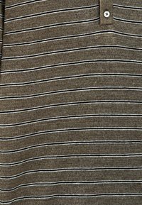 Tissu en tricot marron avec de fines rayures horizontales noires et blanches, et une partie d'un col à boutons visible en haut.