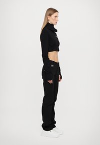 Melna īsā džemperis ar augstu apkakli, saskaņots ar melnām biksēm, ar garām piedurknēm ar pirkstu caurumiem un baltām kedām.