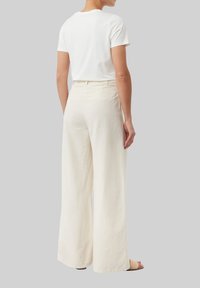 Biała bawełniana koszulka połączona z luźnymi, kremowymi spodniami z lnu. Obuwie ma neutralne, plecione akcenty. Gładka tekstura i swobodny krój.
