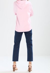 Sudadera rosa con capucha y bolsillo canguro, combinada con jeans de pierna recta de color azul oscuro y sandalias de tacón bloque color marrón claro.