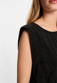 Zwarte ribgebreide top met gestructureerde schouders en een ronde halslijn, voorzien van een textuurdetail in de stof. Close-up van de stof en de vorm.