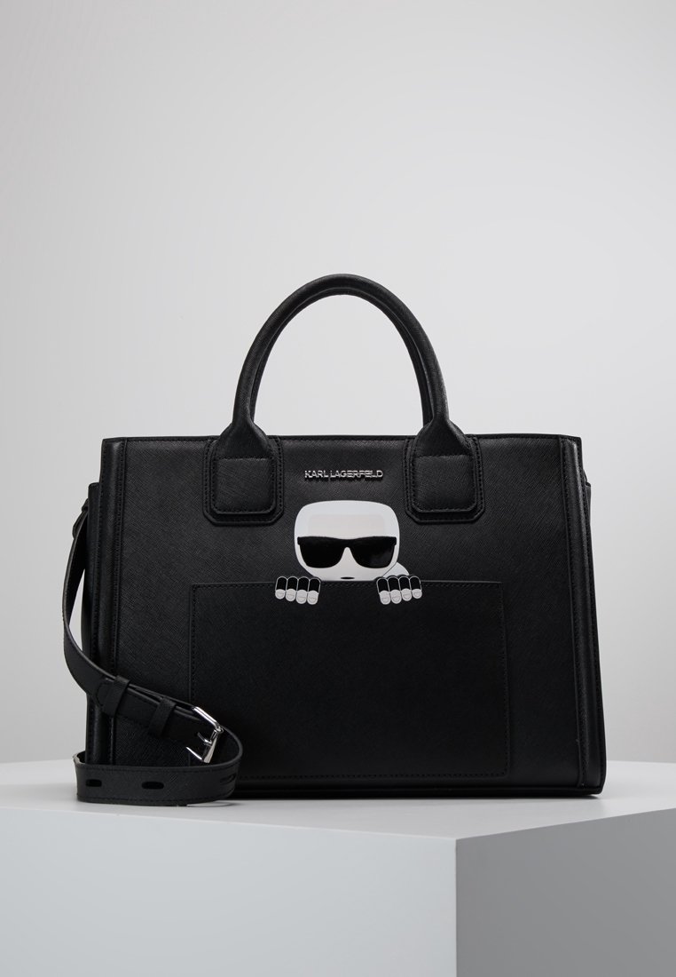 Musta nahkainen käsilaukku, jossa on jämäkkä muotoilu. Laukun etutaskussa on valkoinen sarjakuvahahmo aurinkolasit päässä, ja siinä on irrotettava olkahihna.