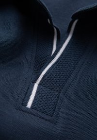 Námořnické polo tričko s texturovaným úpletem, které má bílý pruh podél knoflíkové légy a rozdělený límec pro větší detail.