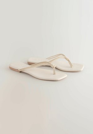Beige flade sandaler med firkantet tå, der har to smalle remme og et mellemrum til tæerne. Glat materiale uden synlige mønstre eller accenter.