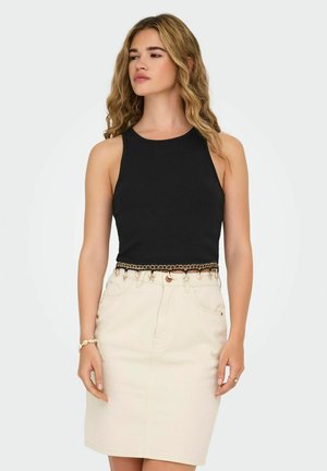 Zwarte mouwloze top met geribbelde textuur; gecombineerd met een crèmekleurige denim rok met een gouden kettingaccent op de taille.