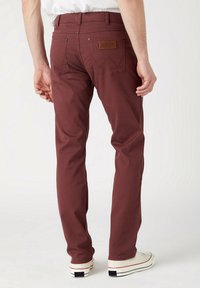 Pantalones de mezclilla burdeos con corte ajustado, que cuentan con dos bolsillos traseros, detalles de costura sutiles y una etiqueta de marca de cuero marrón en la cintura.