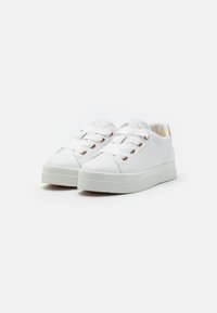 White sneakers featuring a smooth leather exterior, round toe, flat platform sole, and white laces with metallic eyelets.