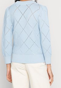 Lichtblauwe gebreide trui met een diamantpatroon met open structuur, geribbelde manchetten en zoom. Gemaakt in een ontspannen pasvorm met gebolde mouwen.