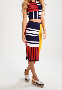 Pletený cropped top a midi sukně s geometrickými červenými, námořnickými, bílými a žlutými pruhy. Má přiléhavý střih a elastický pas.