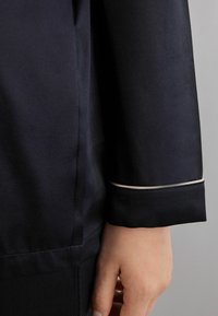 Marinblå satin skjorta med en elegant design, som har en kontrasterande ljus kant vid manschetten, slät textur och åtsittande passform.